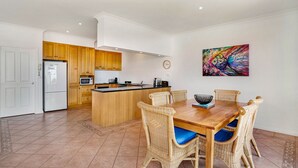 A modern kitchen with wooden cabinets, a central island, and a dining area with wicker chairs and a wooden table. - Cowes Beachfront Penthouse (Cowes)