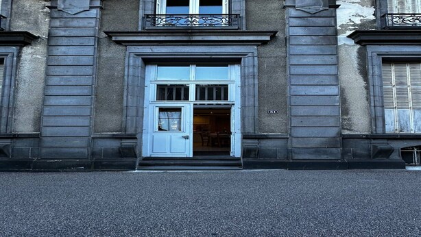 Ein Gebäude mit einem markanten Eingang, der eine weiße Tür und einen kleinen Balkon darüber zeigt.