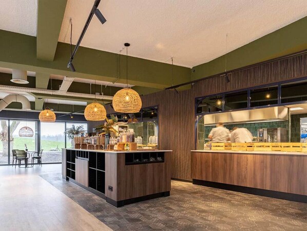 Un restaurant moderne avec un comptoir central, des lampes suspendues en osier et une vue sur l’extérieur.