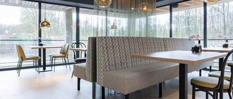 A modern restaurant with a long bench seating area, tables, and hanging pendant lights.