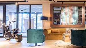 Una sala de estar moderna con una motocicleta, un sillón verde, un sofá y un ventanal con vistas a la ciudad.