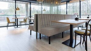 A modern restaurant with a long bench seating area, tables, and hanging pendant lights. - Roomy Retreat with Balcony Perfect for Families Seeking a Quiet Stay (Marknesse)