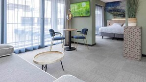 A modern hotel room with a large window, a round table, two chairs, a bed, and a TV on the wall. - Roomy Retreat with Balcony Perfect for Families Seeking a Quiet Stay (Marknesse)