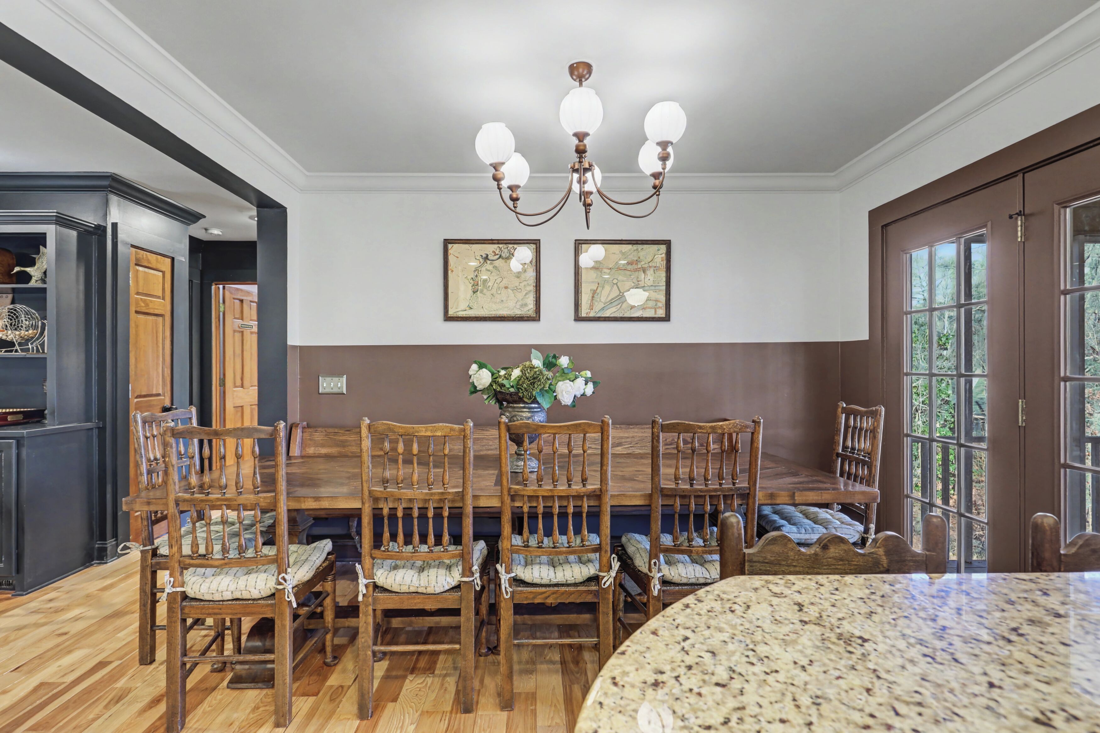 A dining area with a wooden table and chairs, a chandelier, and framed artwork on the wall.