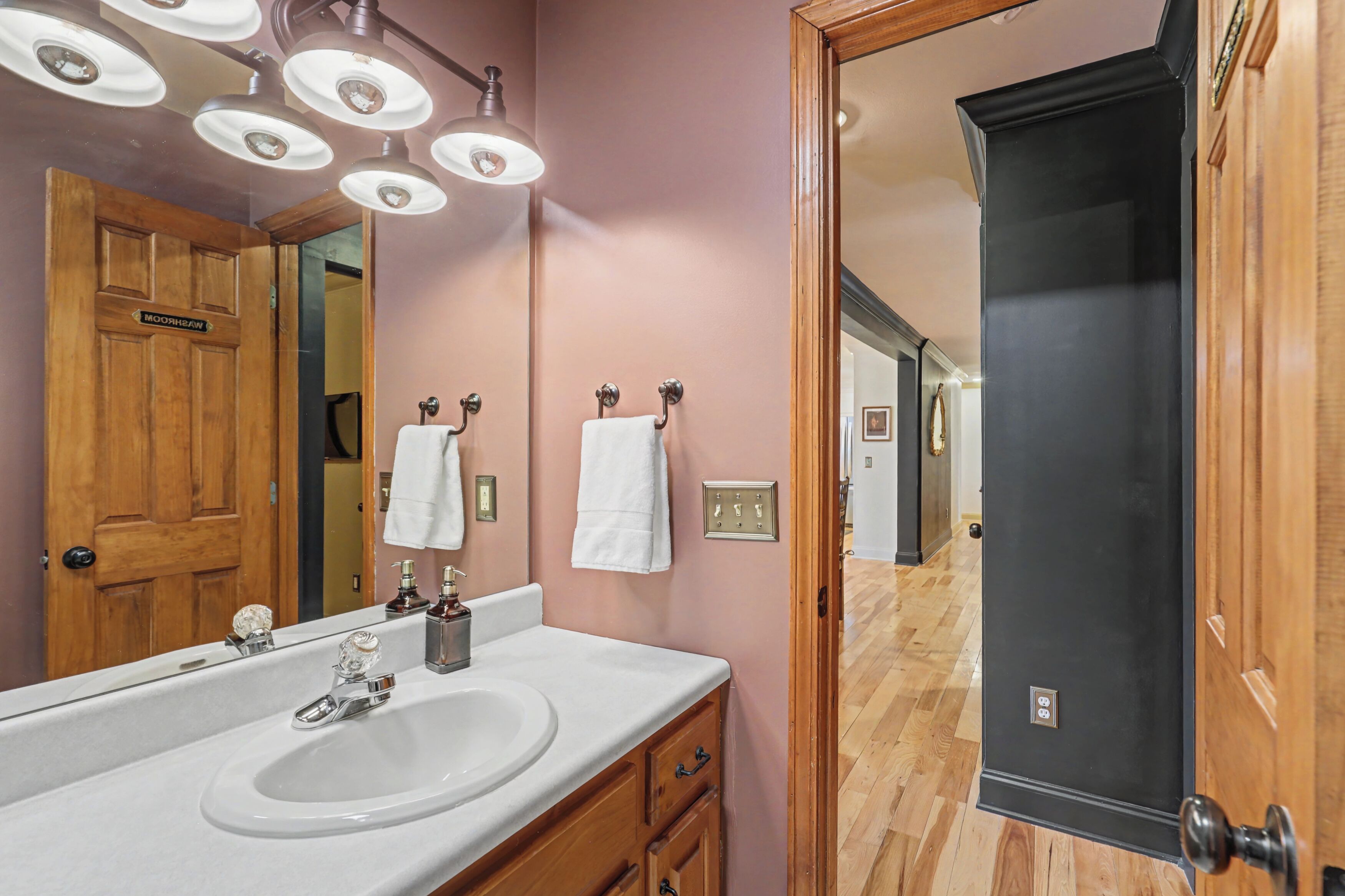 Un baño con una puerta de madera, un lavamanos blanco y un espejo.