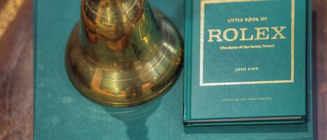 A book titled "Little Book of Rolex" by Josh Sims, placed on a teal book cover titled "The Gardens of Russell Page."