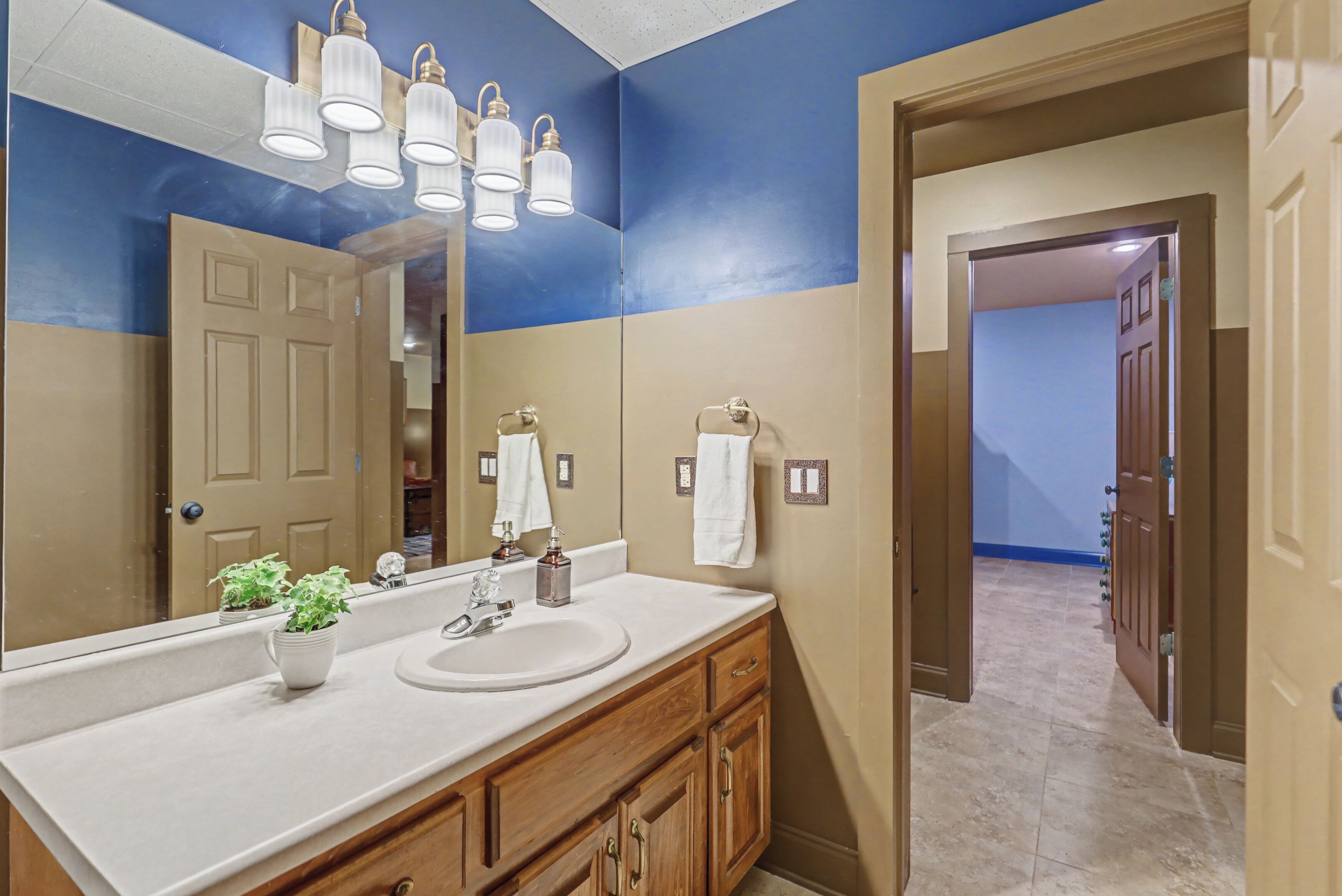 A bathroom with a large mirror, a sink, and a vanity with cabinets. There are two light fixtures above the mirror and a towel rack on the wall.