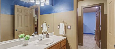 A bathroom with a large mirror, a sink, and a vanity with cabinets. There are two light fixtures above the mirror and a towel rack on the wall.