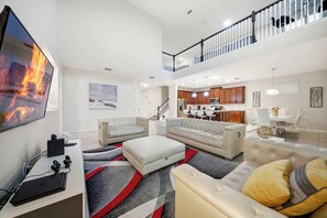 Ein geräumiges Wohnzimmer mit Flachbildfernseher, einer Couch, einem Couchtisch und einer Küche im Hintergrund.