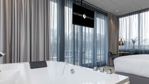 Ein modernes Hotelzimmer mit einer großen, weißen Badewanne, einem Bett und einem Fernseher, der den Namen des Hotels anzeigt.