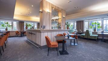 Un moderno bar d'albergo con un'area centrale, posti a sedere e ampie finestre che offrono luce naturale.