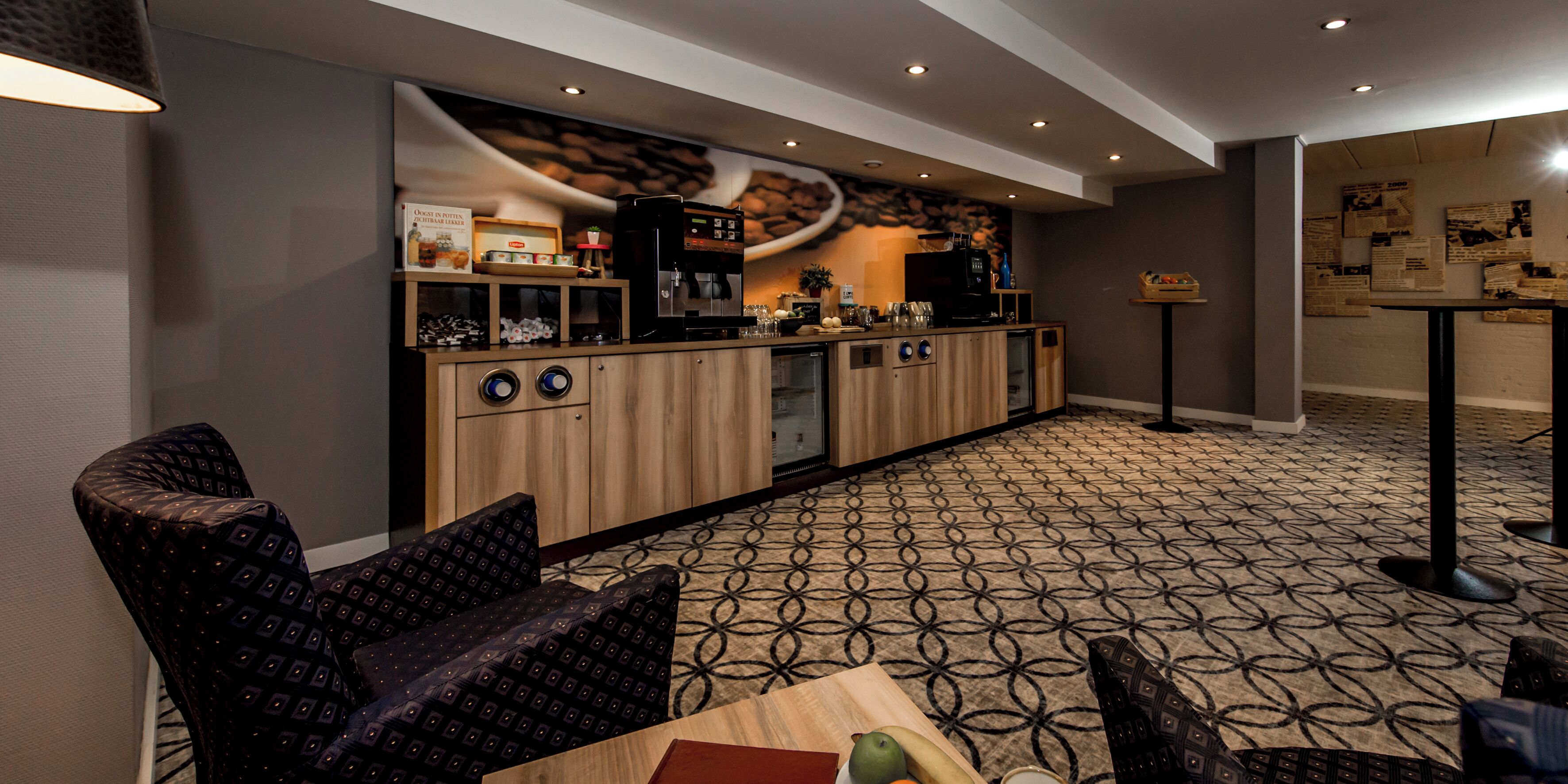 Una hall d'albergo moderna con un angolo caffetteria, area salotto e tappeto a motivi.