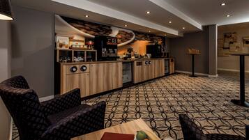 Una hall d'albergo moderna con un angolo caffetteria, area salotto e tappeto a motivi.