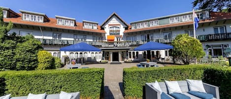 A hotel with a central entrance, outdoor seating area, and a well-maintained garden.