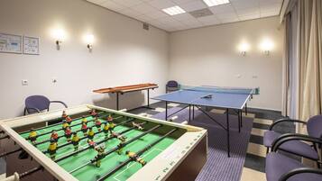 A room with a foosball table, a ping pong table, and several chairs.