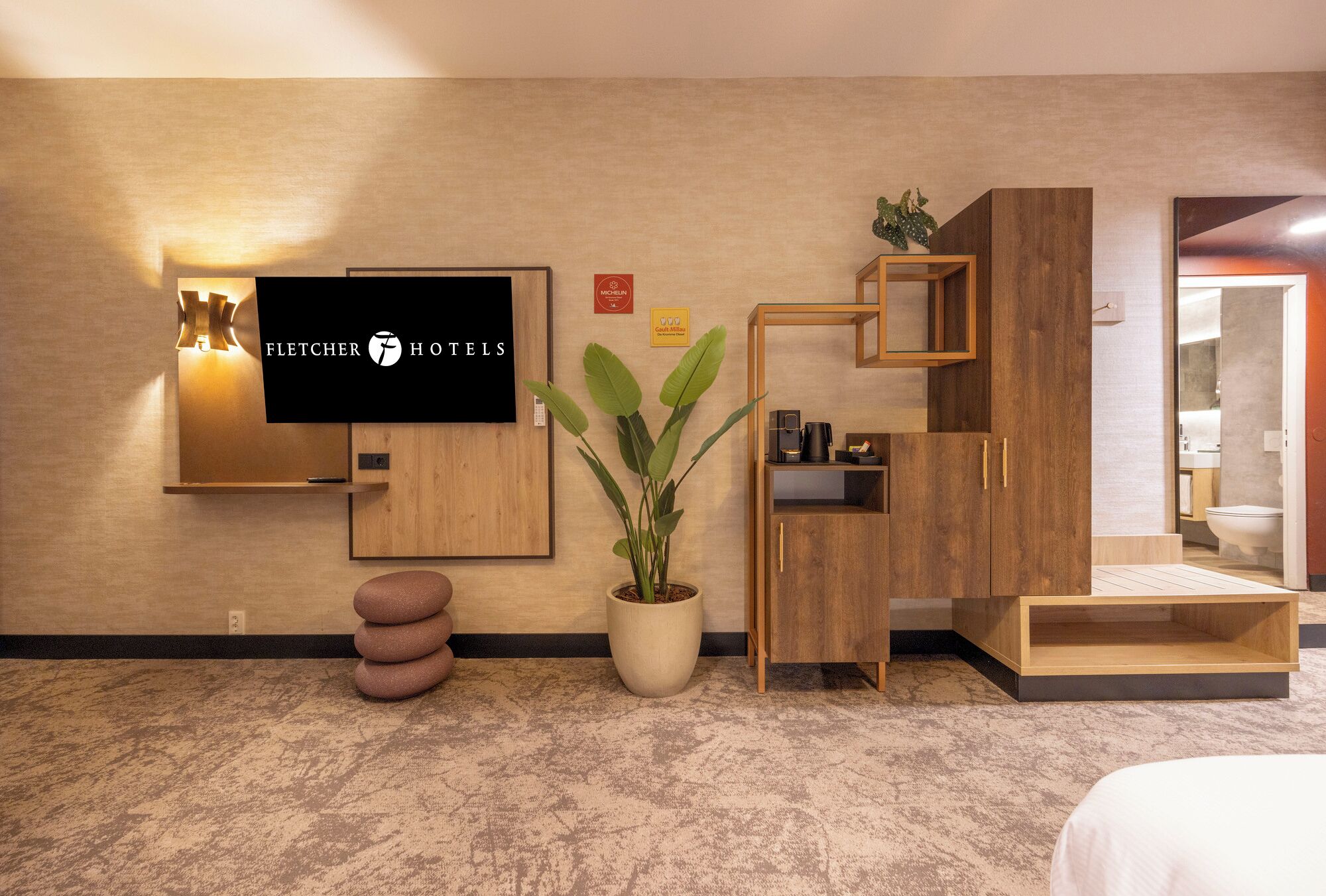 Una habitación de hotel moderna con un televisor de pantalla plana, una planta en maceta, muebles de madera y suelo alfombrado.