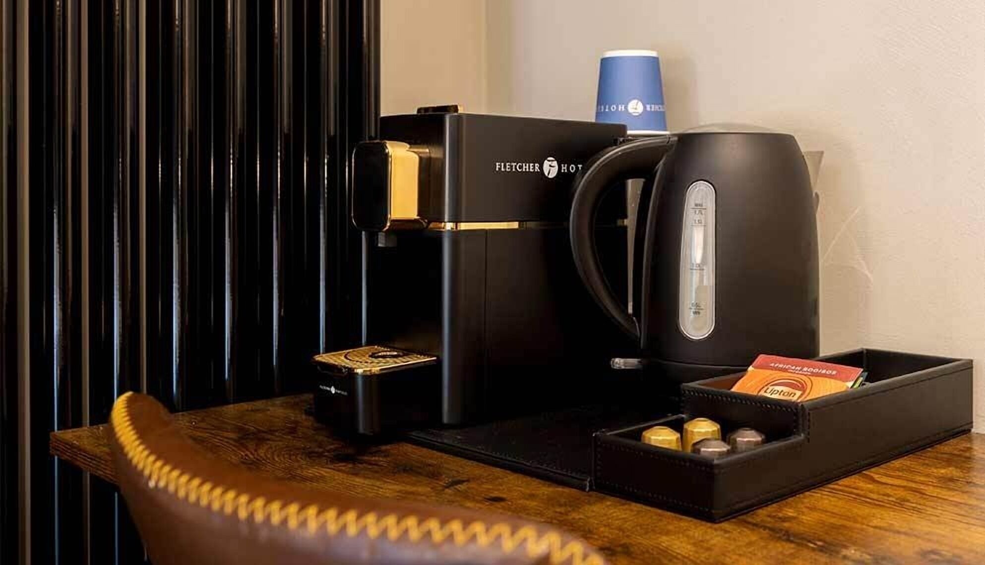 Una cafetera, una taza de café y una caja de cápsulas de café sobre una mesa de madera.
