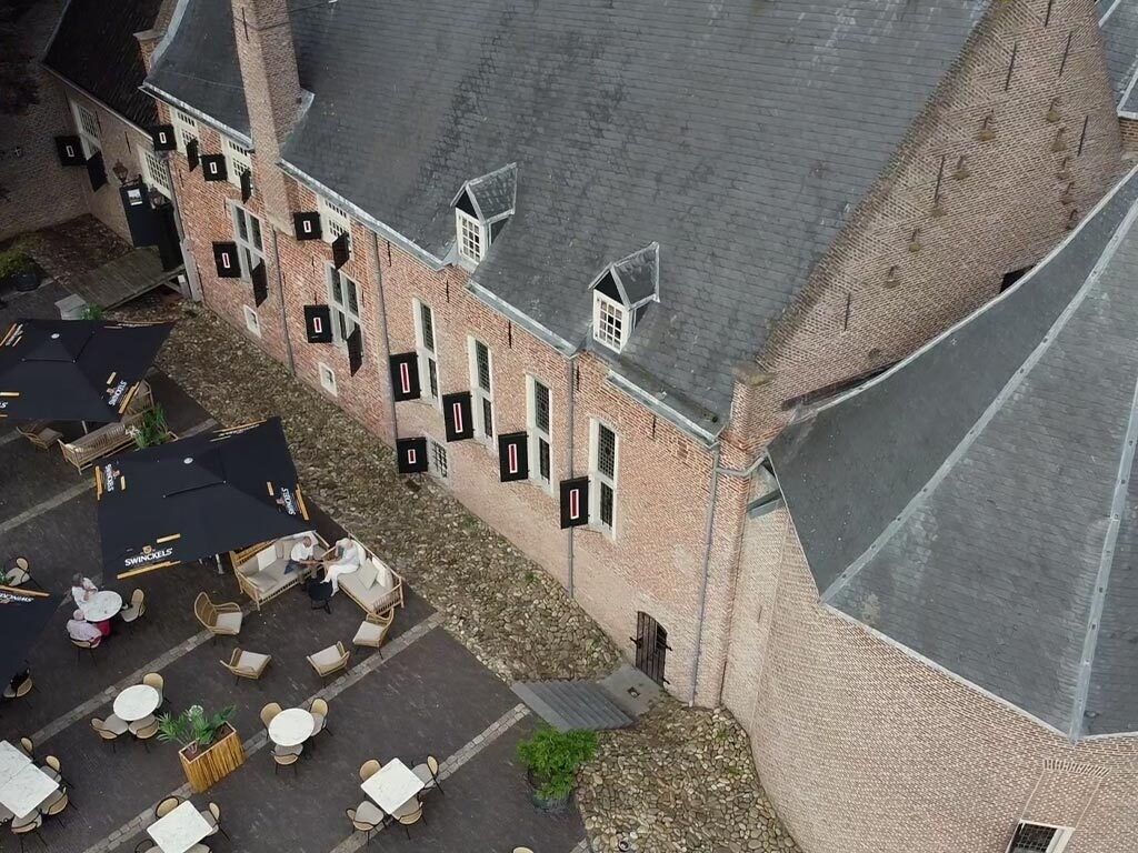 Vue aérienne d’un bâtiment en briques doté de nombreuses fenêtres et d’une cour pavée aménagée avec des sièges extérieurs.