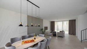 Un espace de salle à manger moderne avec une longue table, des chaises à revêtement gris et des luminaires suspendus.