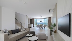 Un salon moderne doté d’un grand téléviseur, d’un canapé, d’un coin repas et offrant une vue sur la mer.