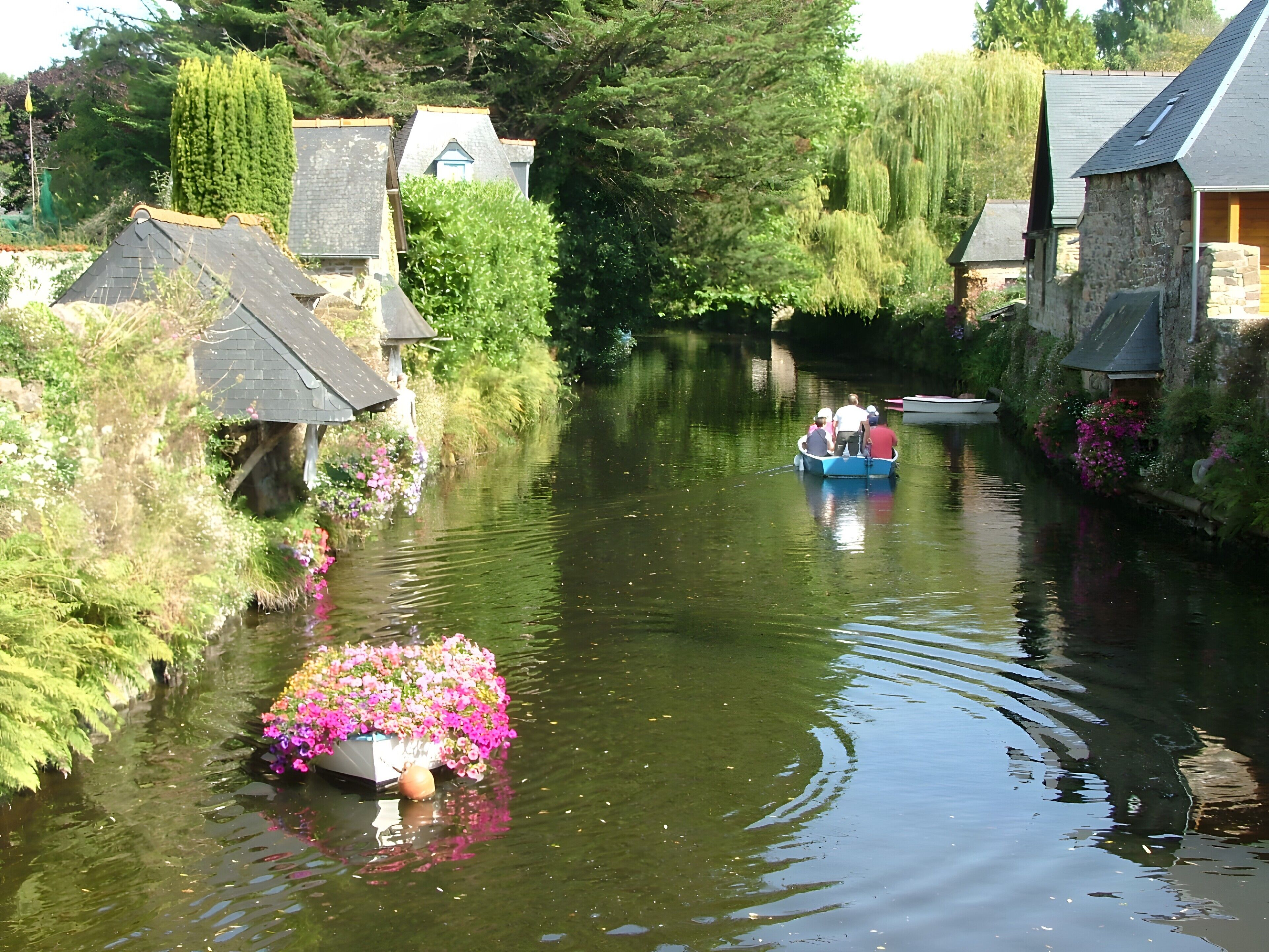 Un canal estrecho con barcos, casas a lo largo de las orillas y una embarcación llena de flores en primer plano.