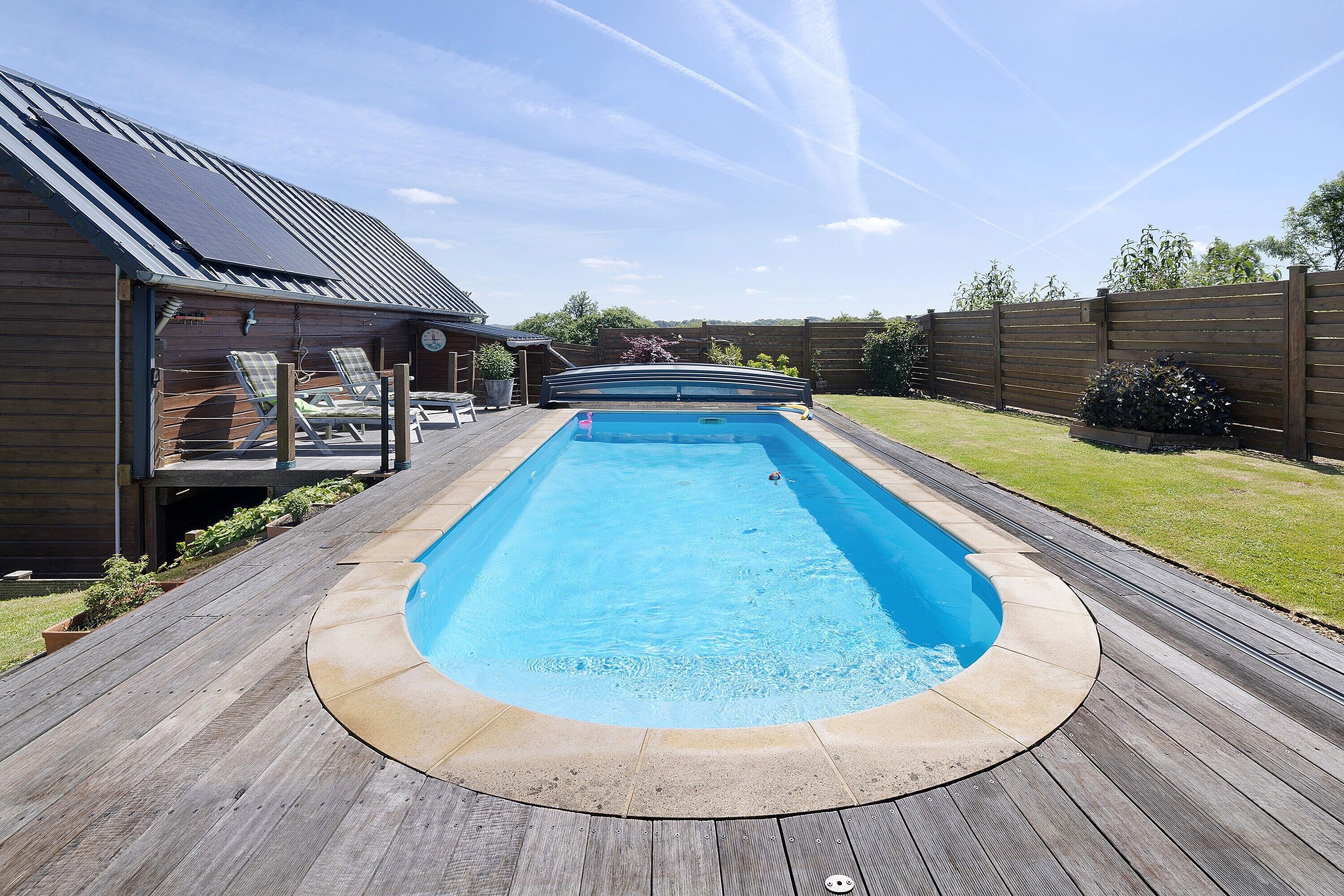 A swimming pool with a wooden deck, a covered area, and a wooden fence.