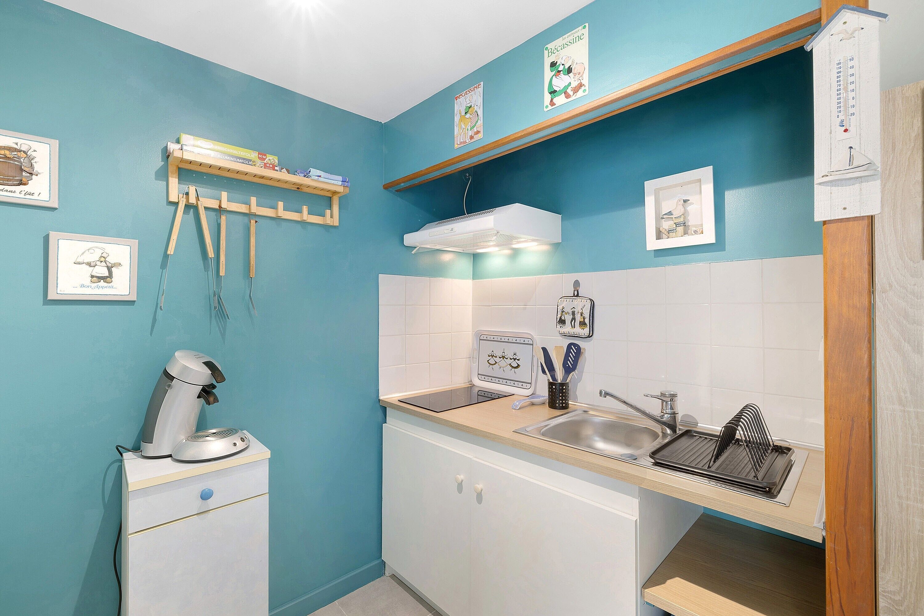 A kitchen with a sink, a coffee machine, a microwave, and a shelf with books.