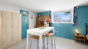 Eine Küche mit einem weißen Tisch, zwei Hocker, einem Schrank und einem Fenster mit Vorhängen.