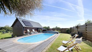 Ein Garten mit Schwimmbecken, Holzterrasse und Liegestühlen.
