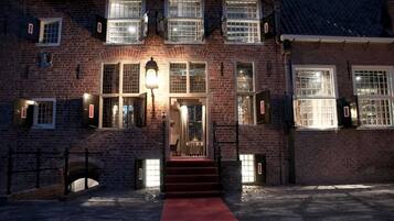 A brick building with a red carpet leading to a door, multiple windows with shutters, and a street lamp.