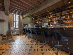 Zona de bar amb sòl de rajola, bigues de fusta al sostre i barra amb tamborets.