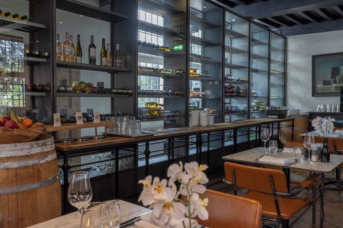 Een restaurantinterieur met een bar, flessenkasten en eettafels.