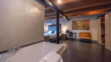 Een moderne hotelkamer met een groot bad, een bed, een bureau en een stoel.