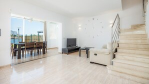 Amplia sala de estar con mesa de comedor, sofá, televisor y una escalera.