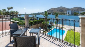 Un balcón con mobiliario de mimbre, una piscina y vistas al mar y las colinas.