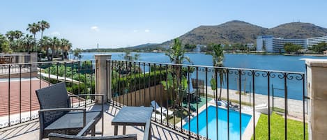A balcony with wicker furniture, a swimming pool, and a view of the sea and hills.