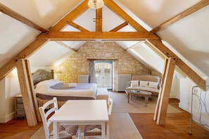 Une chambre avec un mur en pierre, des poutres en bois, un lit, une table et une chaise.
