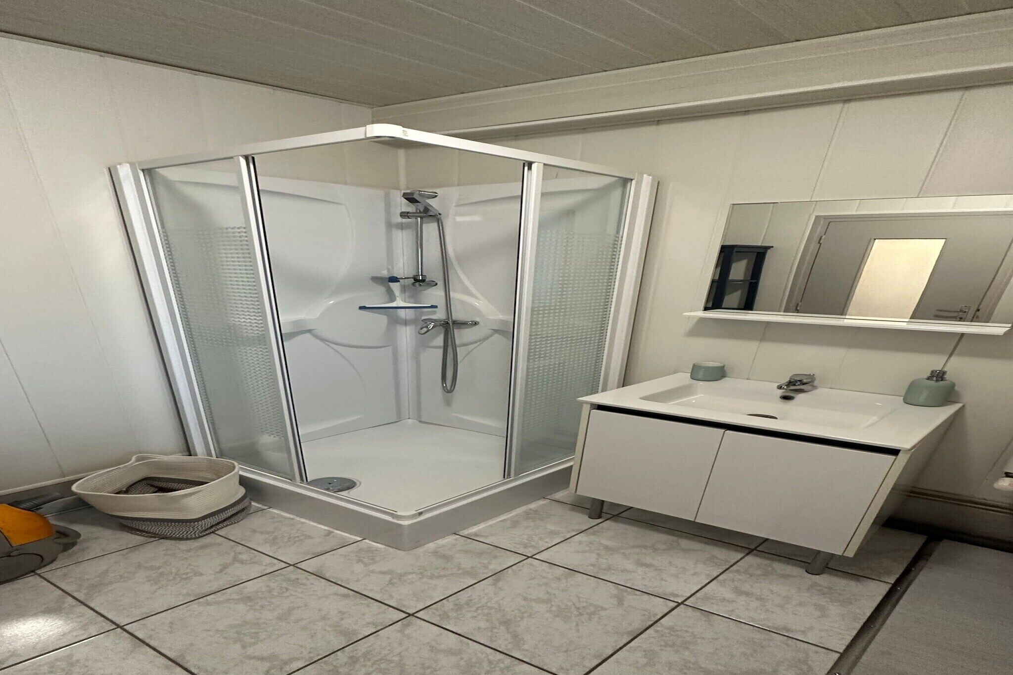 A modern bathroom with a glass-enclosed shower, a white sink with a mirror above, and a small shelf.