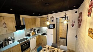 A modern kitchen with wooden cabinets, stainless steel appliances, and a dining area with a patterned tablecloth. - Family Apartment in La Bourboule (La Bourboule)