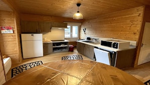 Una cocina compacta con paredes de madera, una mesa de comedor con sillas, un refrigerador, un microondas y un lavamanos.