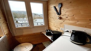 Una pequeña cocina con paredes de madera, una ventana con vistas, un tostador, un hervidor y un portalápices de pared.
