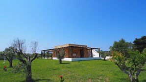 A small, single-story building with a stone facade and a flat roof, surrounded by a grassy area with trees.