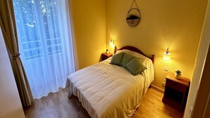 Une chambre à coucher avec un lit, deux lampes de chevet, un miroir fixé au mur et une fenêtre avec des rideaux.