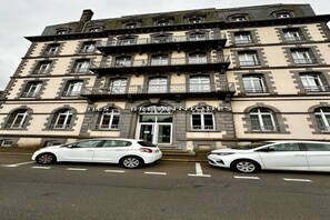 Ein mehrstöckiges Gebäude mit der Aufschrift "LES BRITANNIQUES", das ein Hotel kennzeichnet. Vor dem Gebäude befinden sich zwei weiße Autos.
