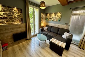 A cozy living room with a stone wall, a sofa, a glass coffee table, and a wooden floor. - 2-Bedroom Valley View Duplex (Mont-Dore)