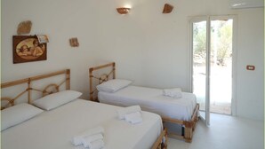 Une chambre avec deux lits en bois, du linge de lit blanc, un tableau accroché au mur et une porte donnant sur un espace extérieur.