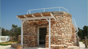 Une structure en pierre surmontée d’une pergola en bois, avec une porte et des marches menant à l’entrée.