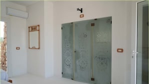 Une pièce avec un mur blanc, un miroir et une porte en verre ornée de motifs décoratifs.