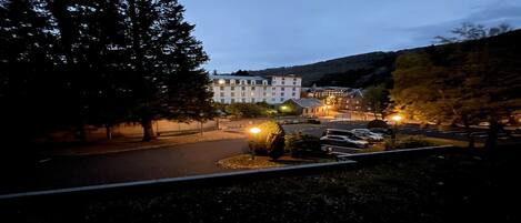 Ein Hotel mit Parkplatz, Bäumen und Bergen im Hintergrund.