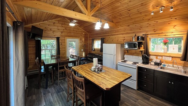 Interior de una cabaña de madera con cocina, comedor y un ventanal grande.